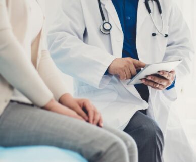 a image of a doctor sitting on a patient bed with only their abdomin showing as he writes a prescription on a paper prescription pad