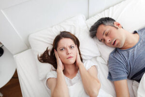 Woman covering ears, annoyed by the snoring of her husband